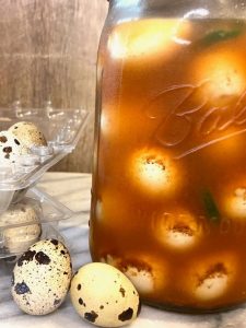 glass jar with pickled eggs inside and small quail eggs sitting next to it