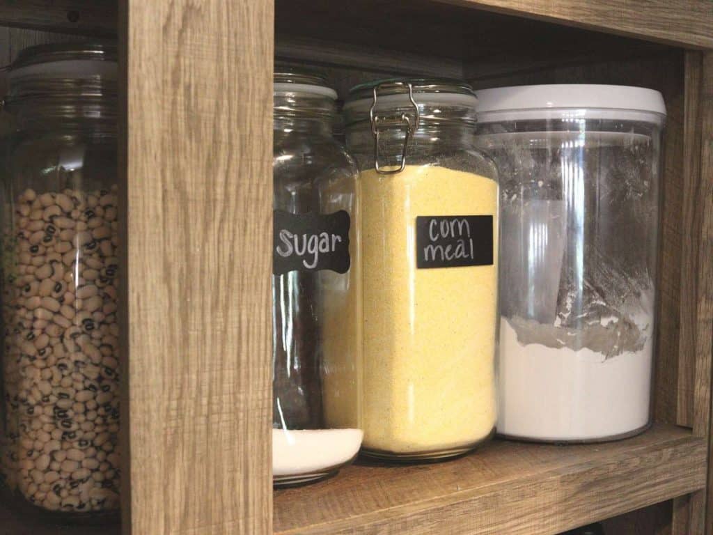 open pantry with glass jars of corn meal, sugar, flour and dried peas