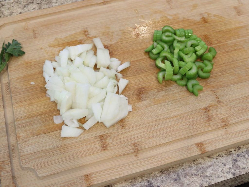 DICED ONION AND CELERY ON WOODEN CUTTING BOARD