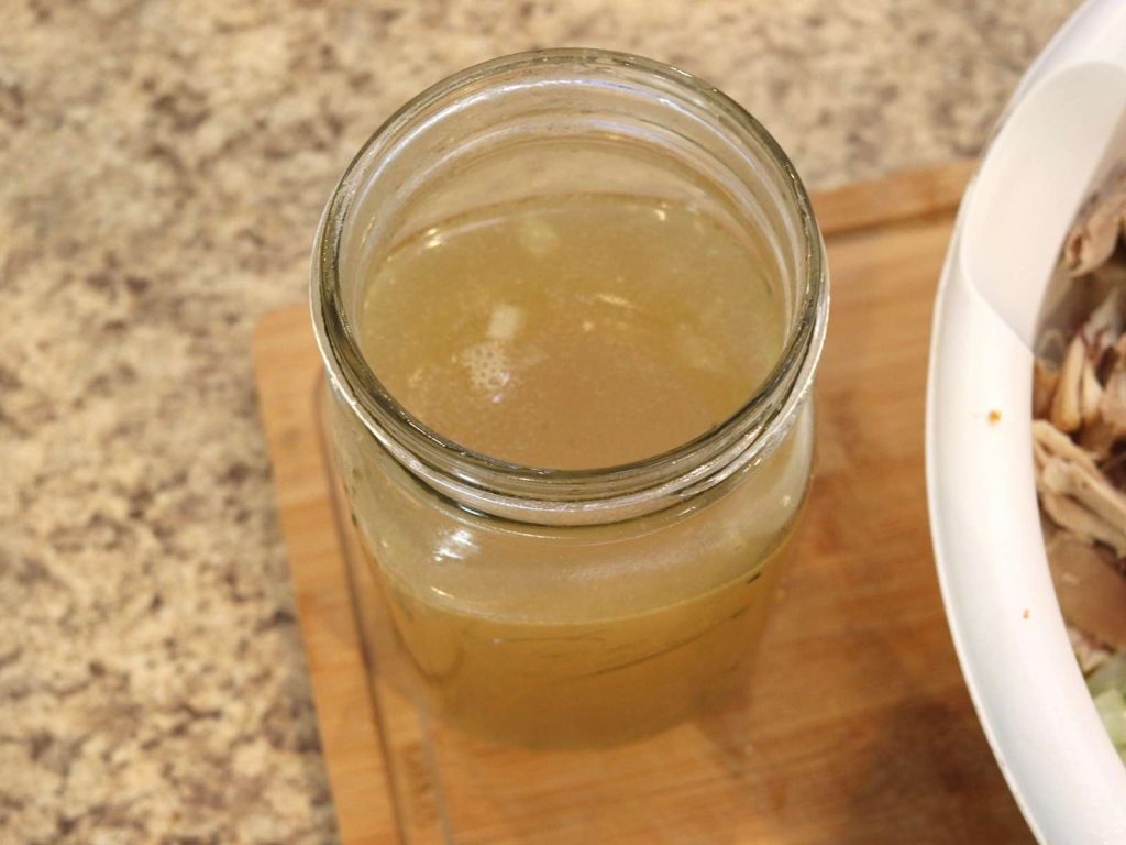 GLASS MASON JAR WITH CHICKEN BROTH IN IT SITTING ON WOODEN CUTTING BOARD