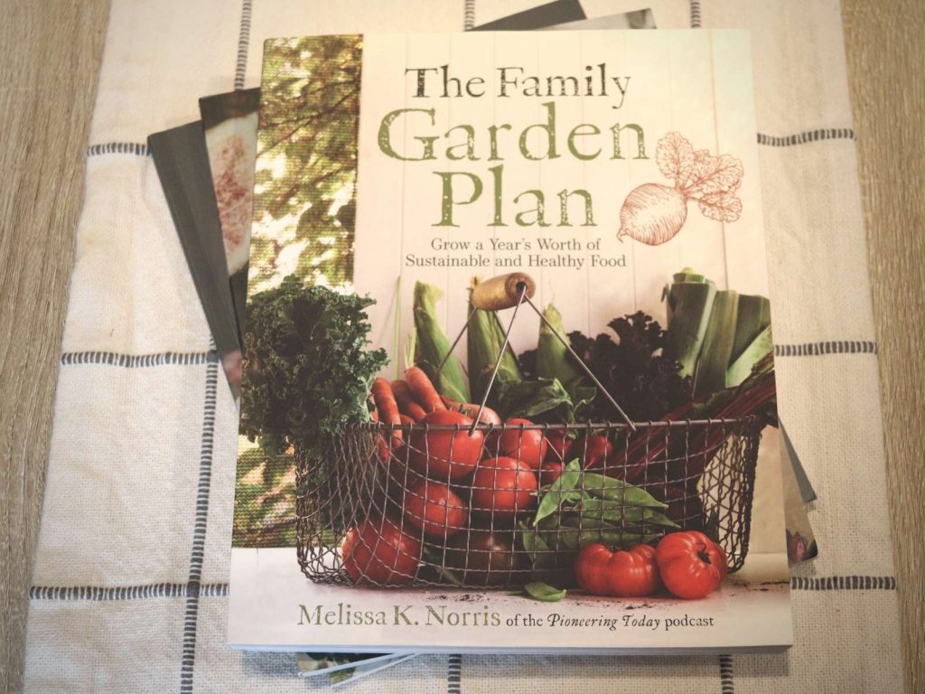 stack of homesteading books on table with The Family Garden Plan book on top