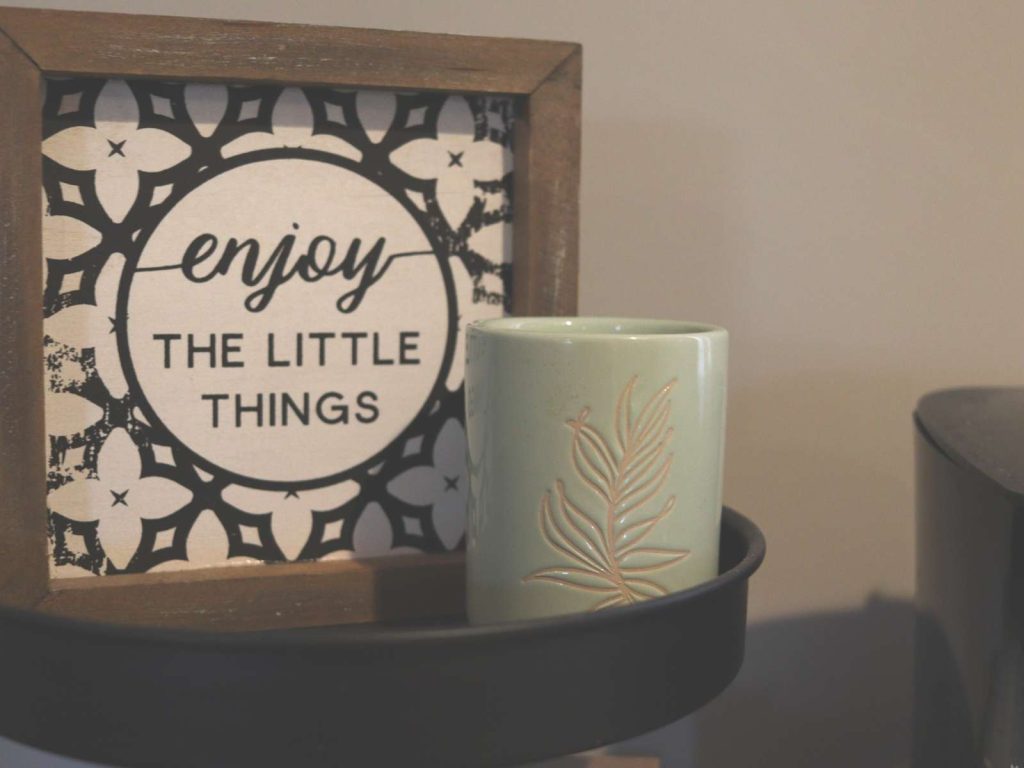 sign that says enjoy the little things sitting next to a candle