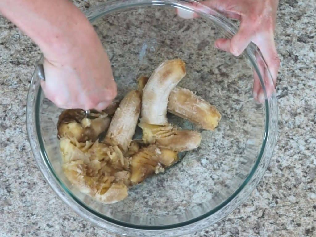 glass bowl with bananas in it being mashed with a fork