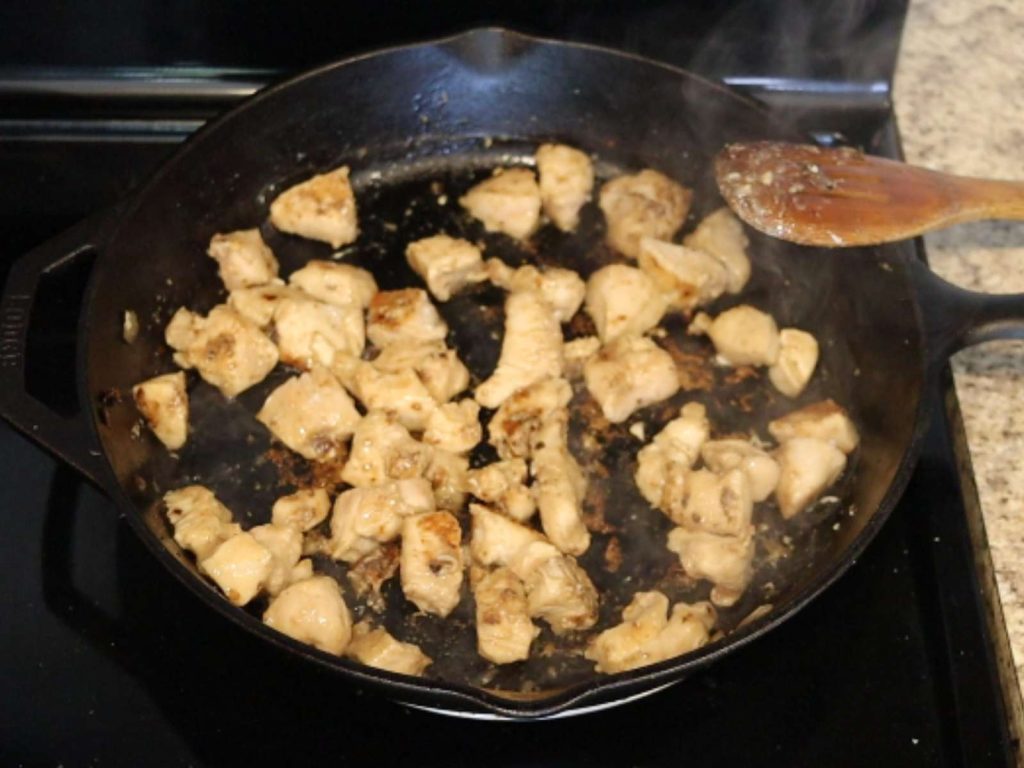 chicken pieces cooking in cast iron skillet