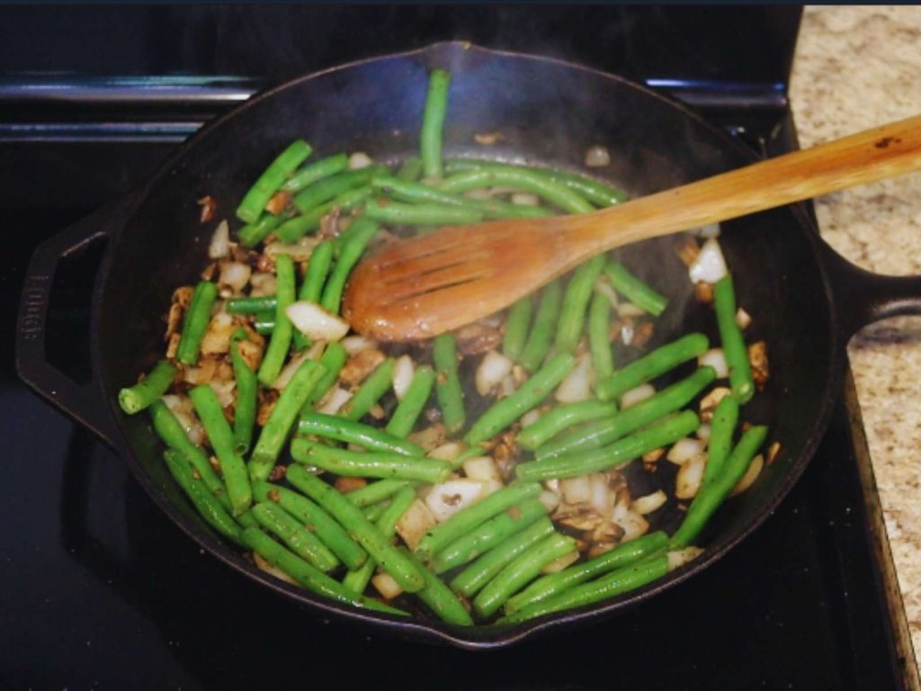 green beans, onions, and mushrooms cooking in cast iron skillet