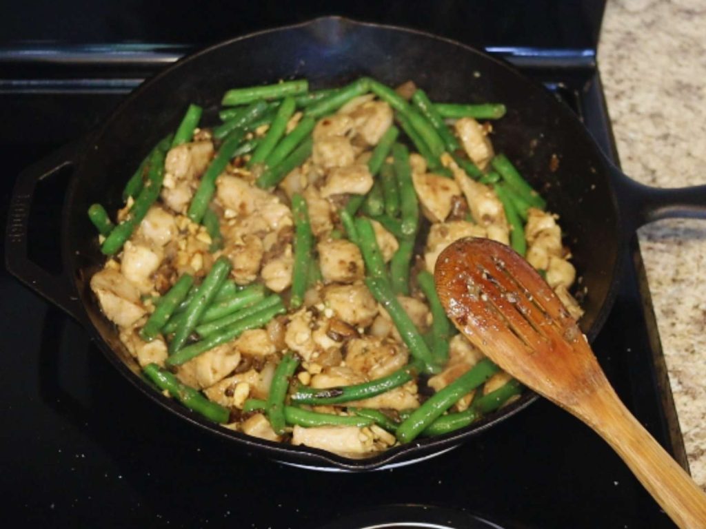 cashew chicken with green beans and mushrooms in skillet with wooden spoon