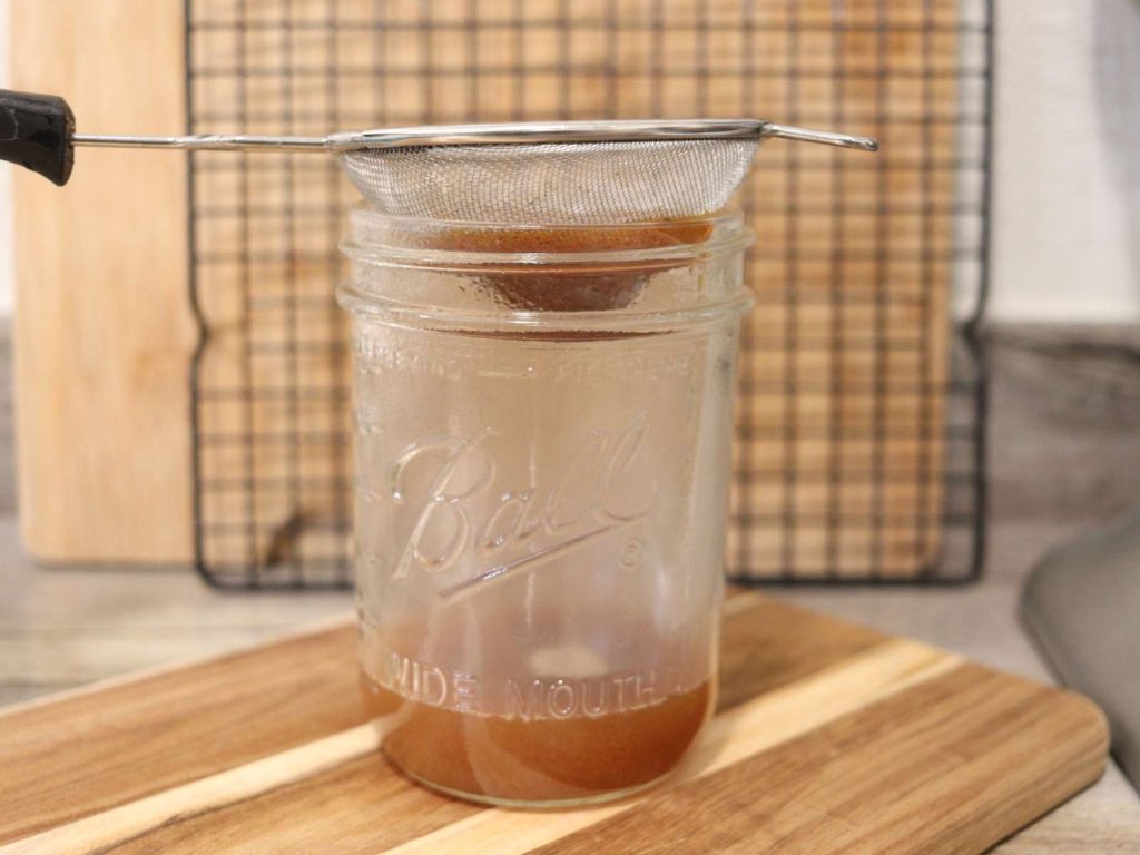 pint size mason jar with a fine mesh strainer over it, full of pumpkin spice syrup