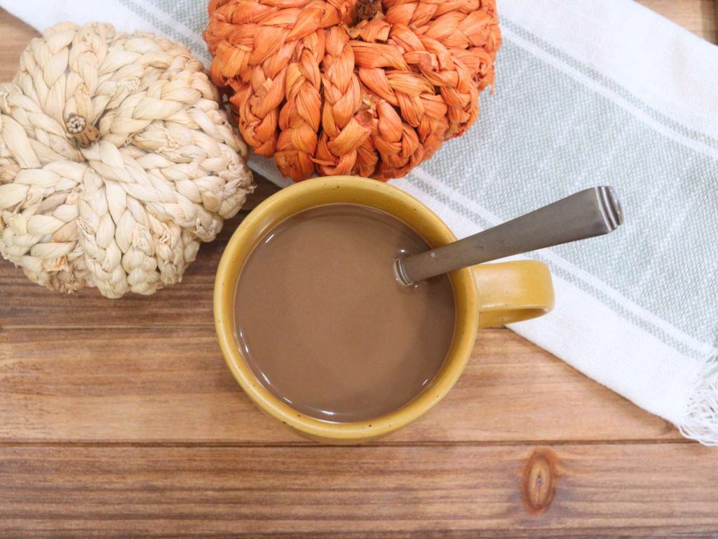 homemade pumpkin spice latte in yellow coffee cup next to wicker pumpkin decor