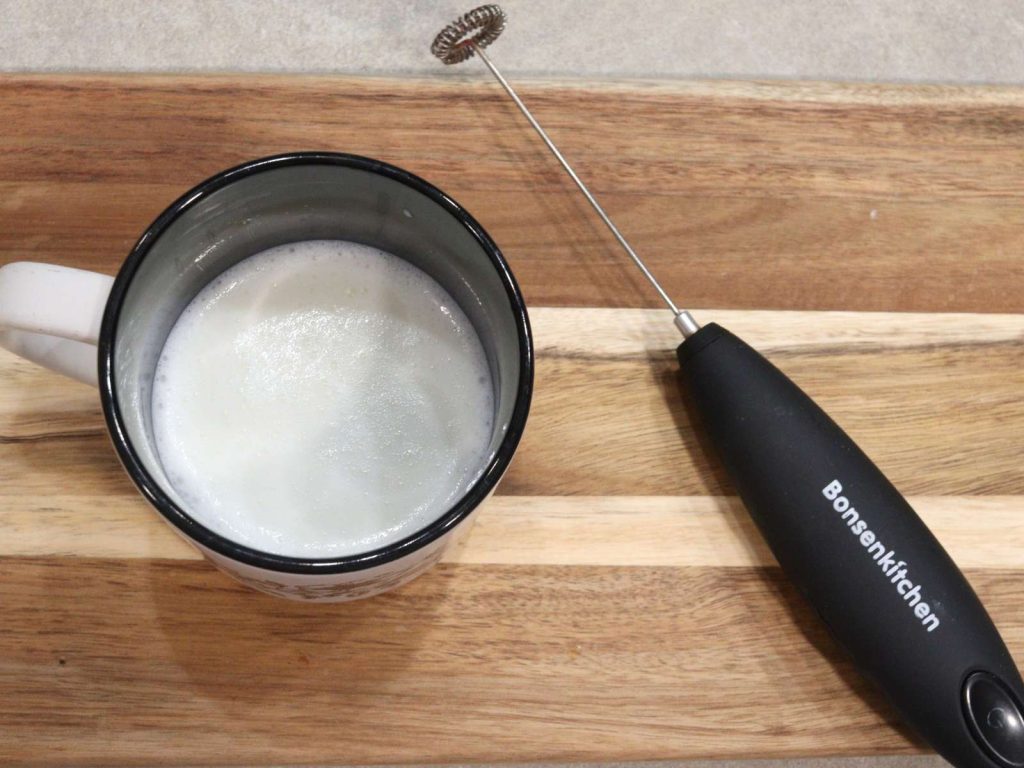 milk frother to sitting next to cup of frothed milk
