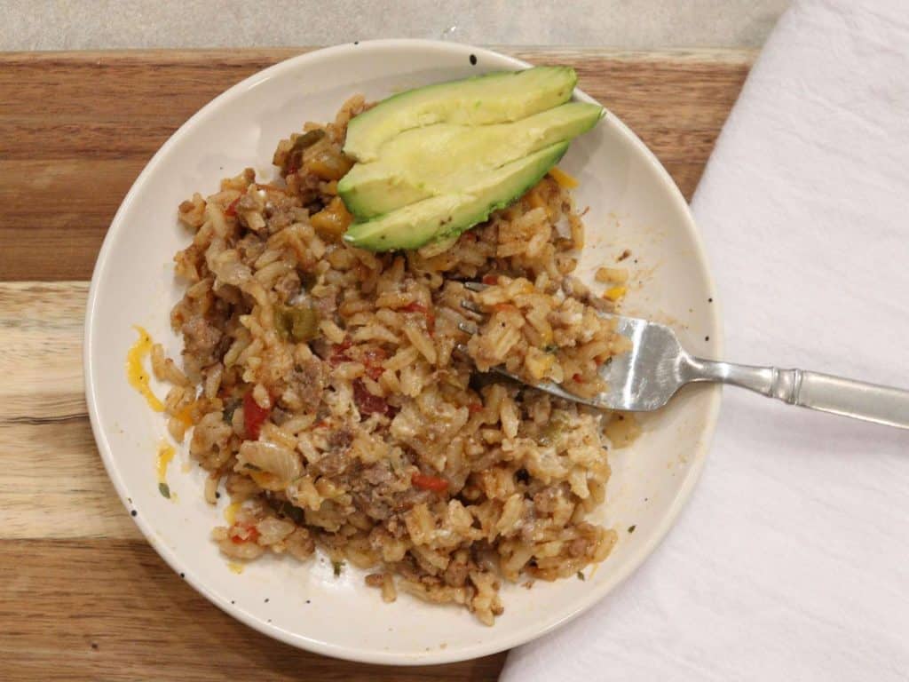 cheesy mexican rice on small white plate with sliced avocado