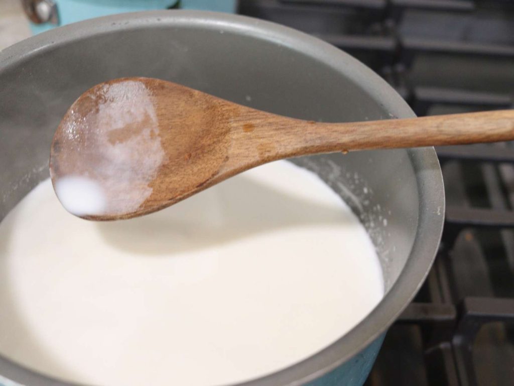 homemade peppermint creamer in a small sauce pan being stirred with a wooden spoon