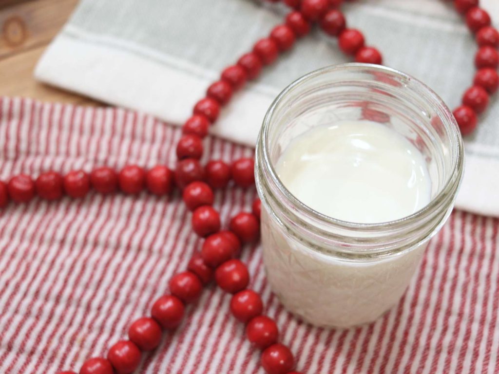 glass jar with homemade creamer sitting on red and white cloth with red wooden beads