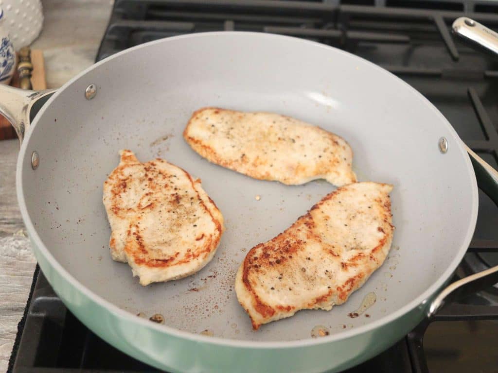 nonstick green skillet on stovetop with chicken breasts cooking