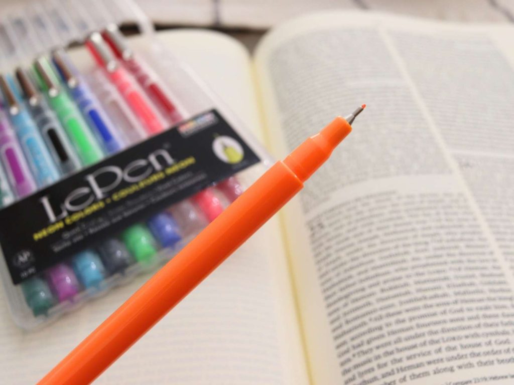 orange pen with fine tip sitting in front of bible