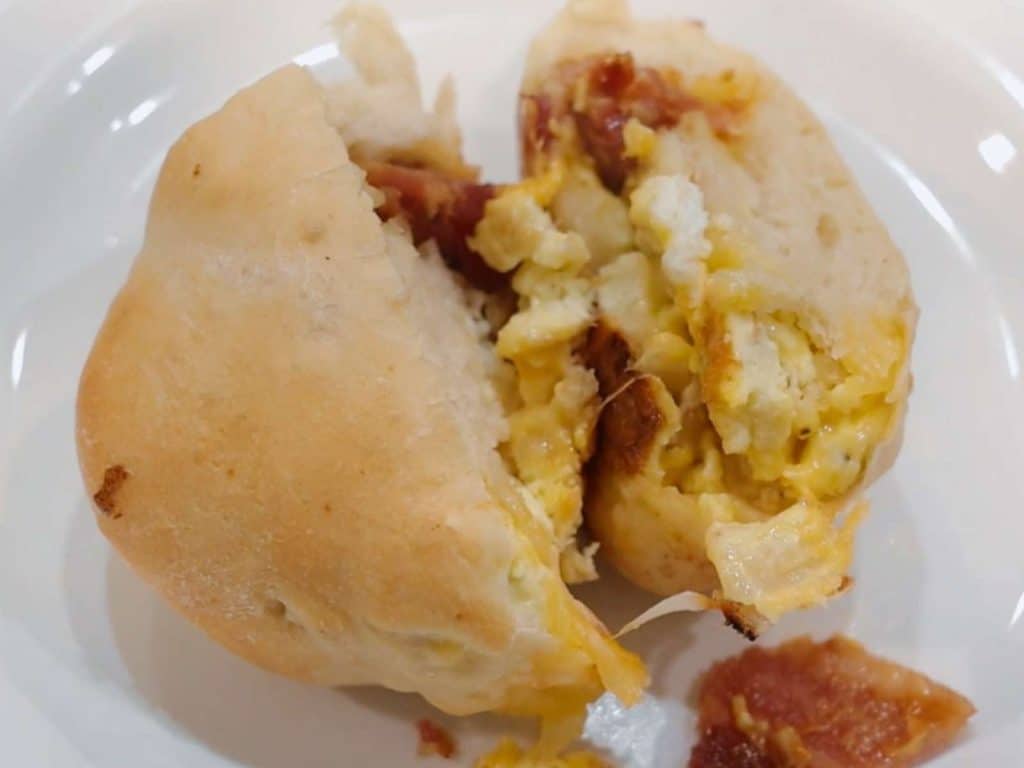 breakfast calzone with eggs, bacon, and cheese cut open on white plate