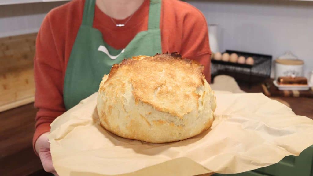 round loaf of artisan bread sitting on parchment paper being held by woman in green apron