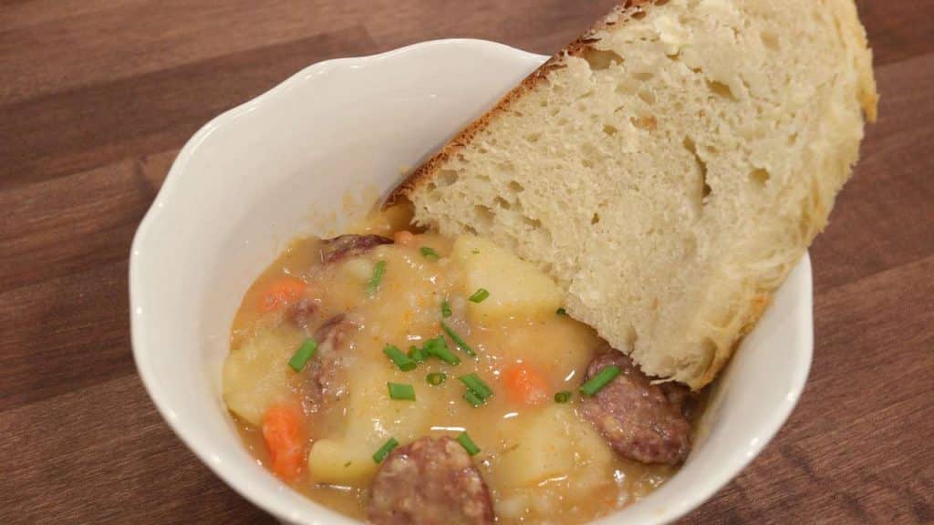 slice of bread in white bowl with sausage and potato soup