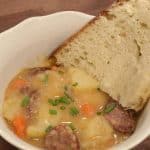 sausage, potatoes, and carrots in a white bowl with slice of bread