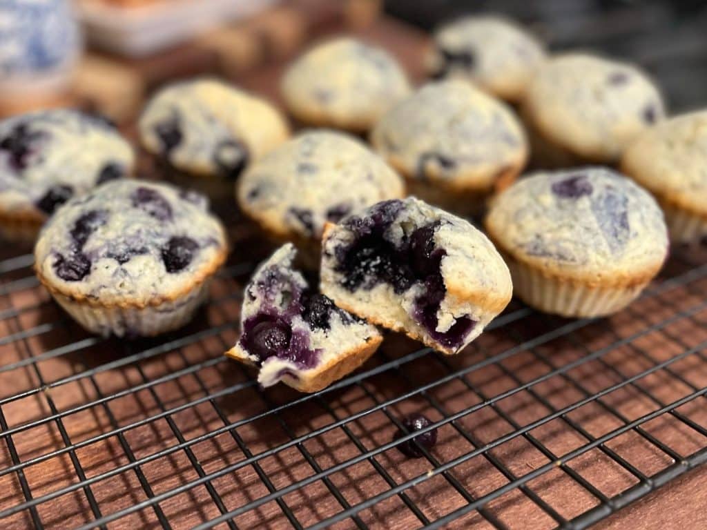 blueberry muffin broken open on cooling tray with more muffins behind it