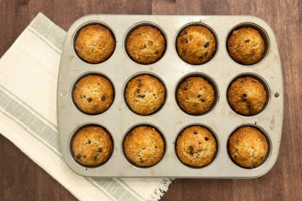 chocolate chip banana muffins in a muffin tin on wooden counter