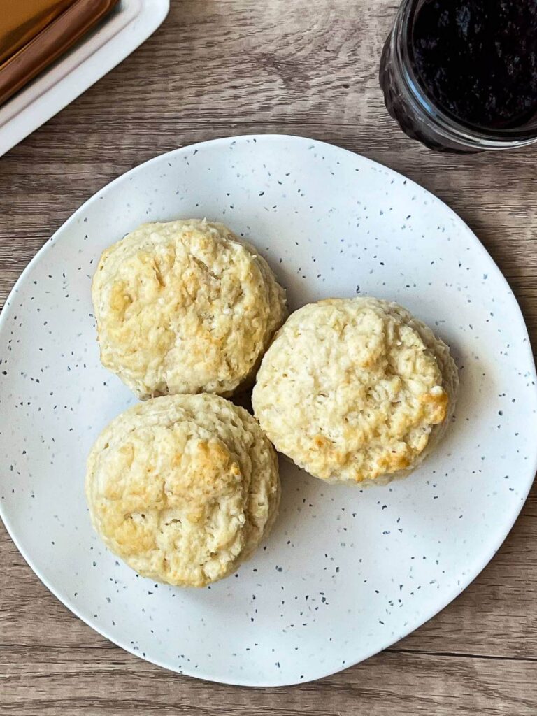 3 buttermilk biscuits sitting on a white plate on a wooden background