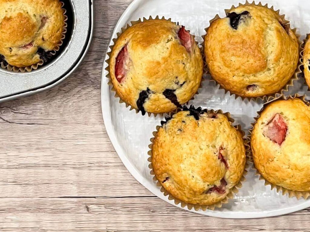 muffins with blueberries and strawberries in them sitting on a white plate