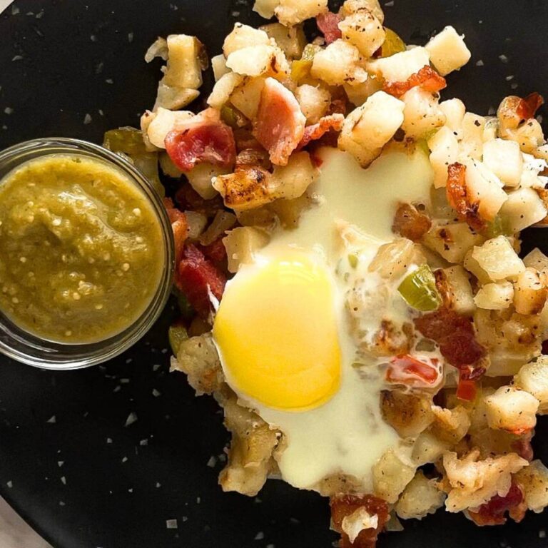 diced hashbrowns with bacon and egg sitting on a black plate with salsa verde