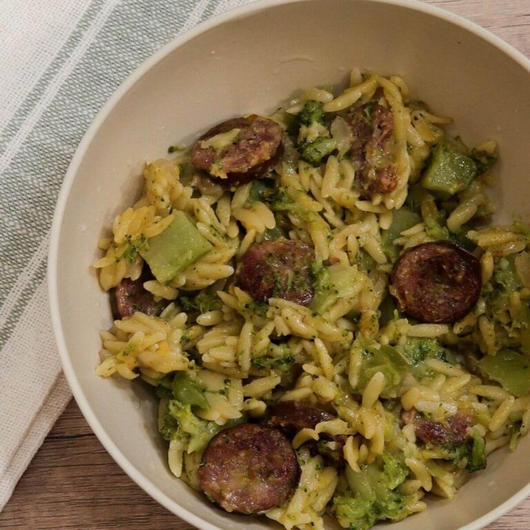 tan bowl with cheesy orzo with smoked sausage and small pieces of broccoli
